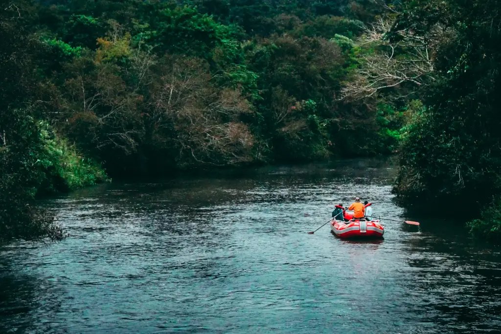 Multiple people in helmets and life jackets paddling a yellow raft through white water rapids