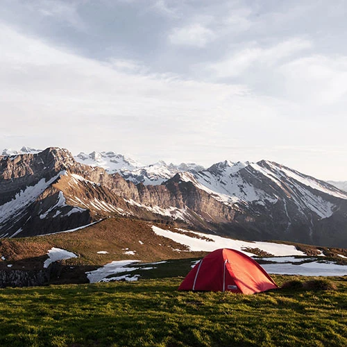 Tent set up in a mountain clearing surrounded by tall pine trees with distant peaks in the background under a clear sky creating a peaceful and inviting atmosphere for outdoor adventure