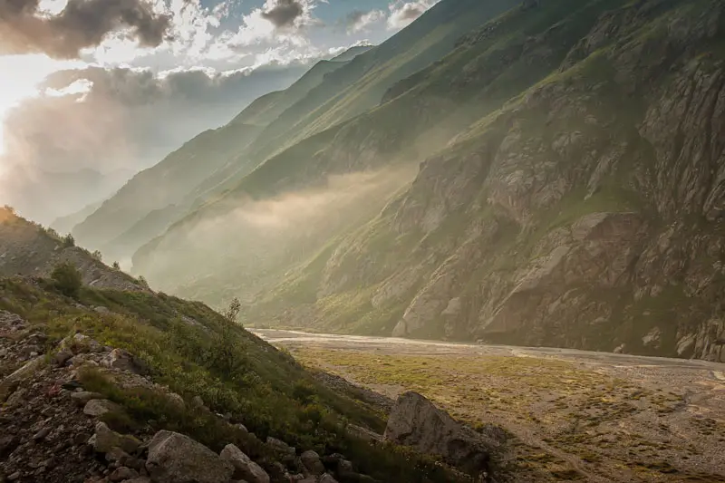 Misty mountain peaks rising above a forested landscape with soft clouds drifting around the summits creating a calm and peaceful atmosphere