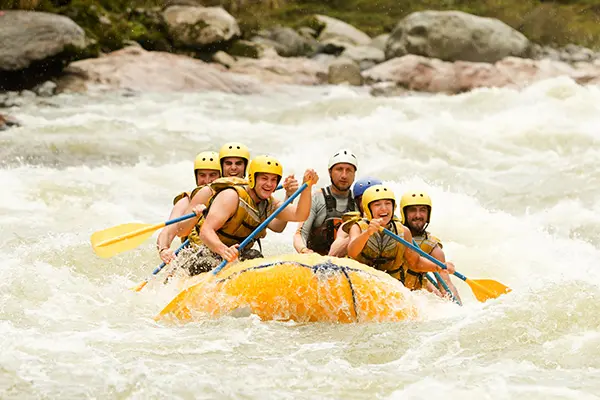 Group of people wearing yellow helmets and life jackets paddling a yellow raft through whitewater rapids with splashing water and rocky riverbanks in the background conveying excitement and teamwork in an adventurous outdoor setting